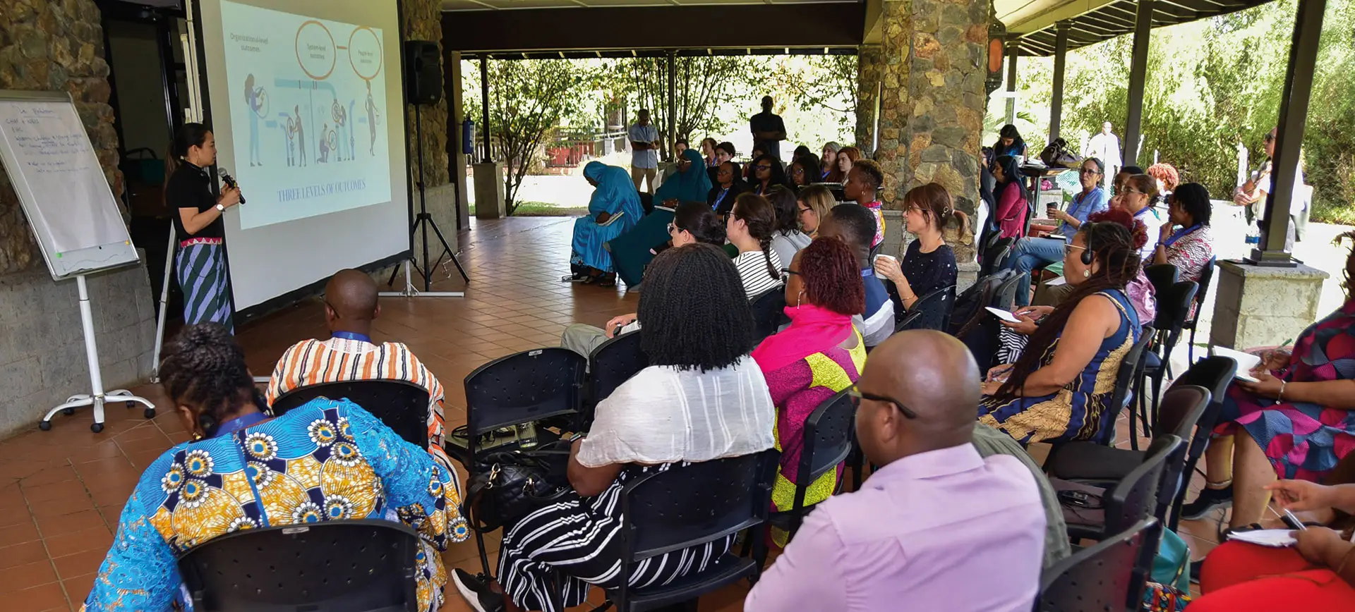 A person giving a presentation in front of a group of people seated in an open space | Co-Impact.