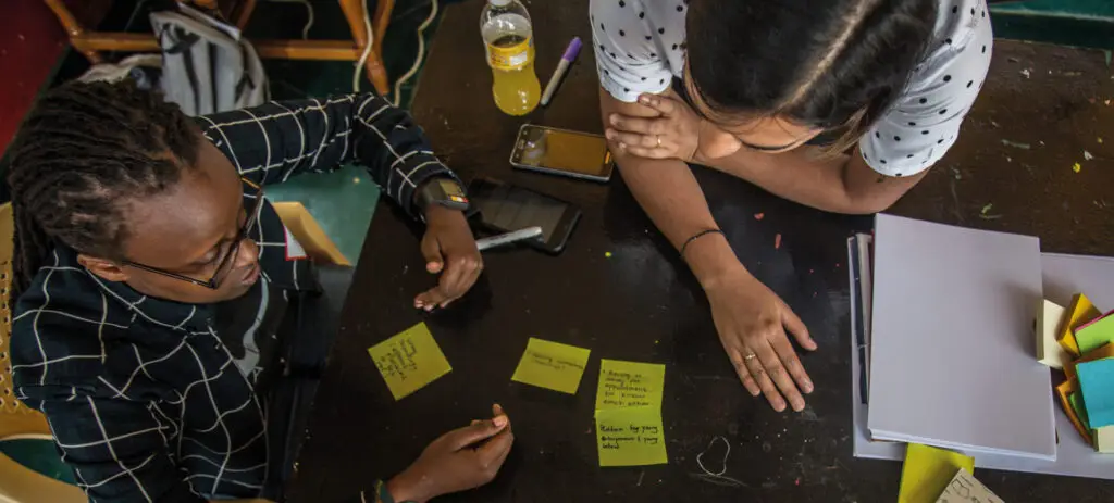 Aerial view of two people working at a table with yellow sticky notes | Co-Impact.