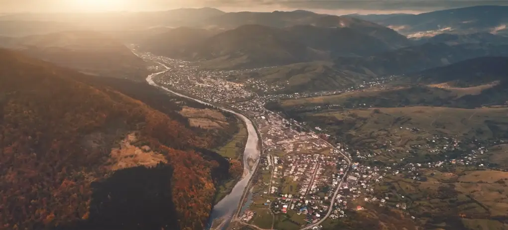 Aerial view of a valley with a river and a town surrounded by mountains at sunset | Co-Impact.Aerial view of a valley with a river and a town surrounded by mountains at sunset | Co-Impact.