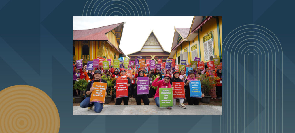 Women holding colorful protest signs in Indonesian language during rights demonstration in front of traditional yellow buildings