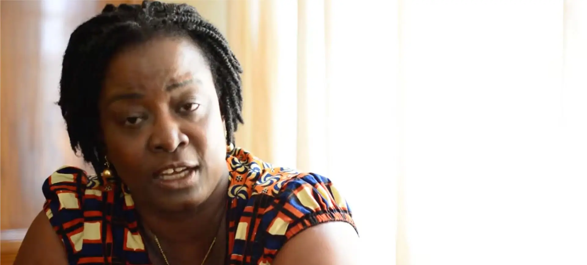 Woman with braided hair speaking, wearing colorful traditional African-style patterned clothing