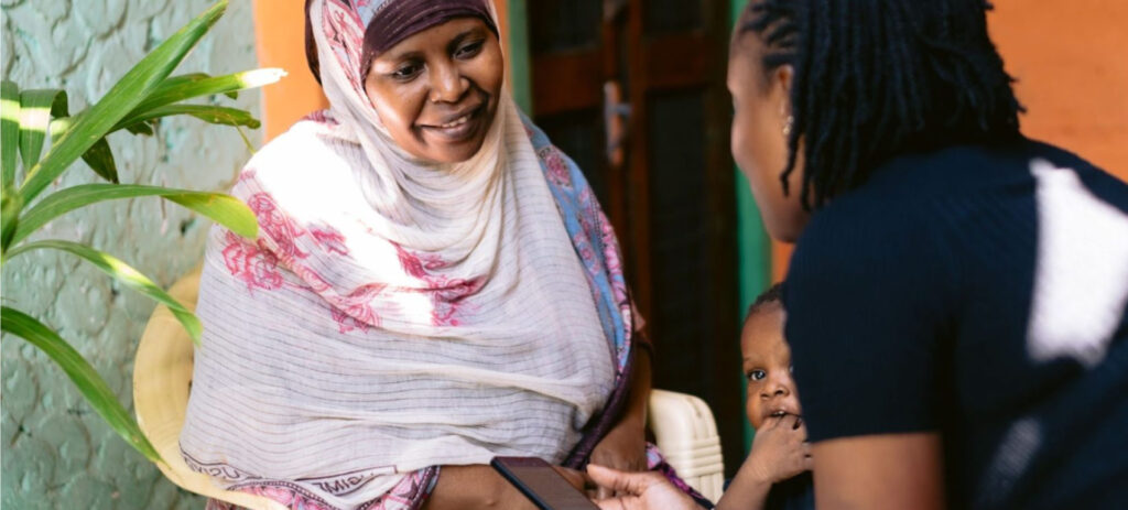 Smiling woman in colorful headscarf talking with another woman holding a child in home setting