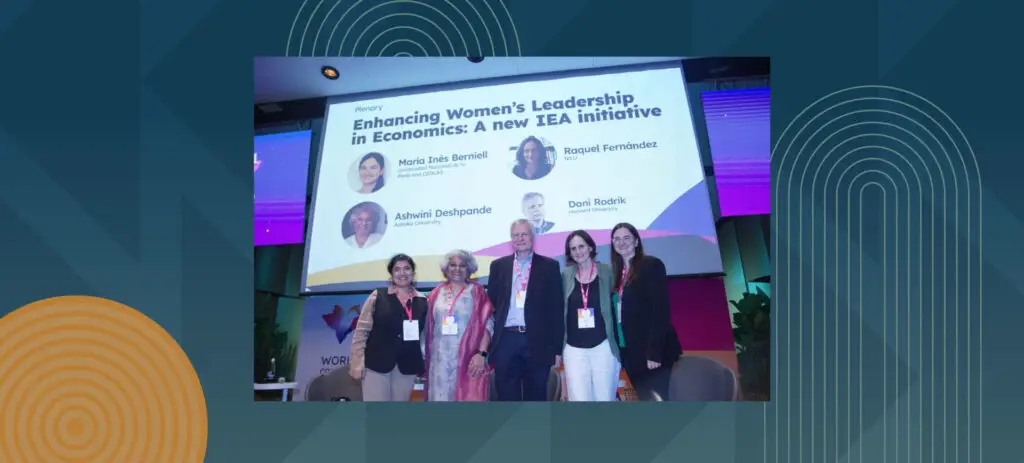 Five panelists posing at women's leadership conference with presentation screen showing IEA initiative speakers