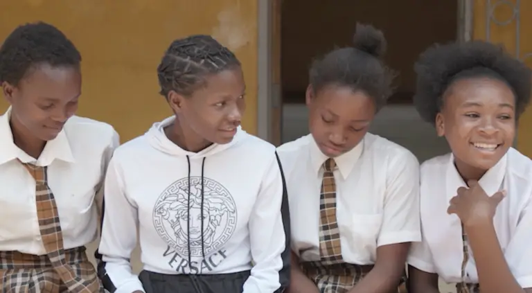 Schoolgirls in uniform sitting together outside a classroom on the Co-Impact website.